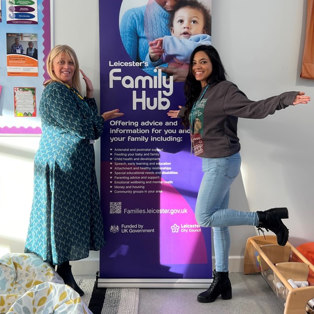 Two women standing next to a poster promoting family hubs1